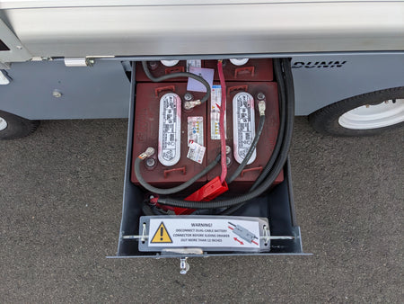 Open battery compartment showing two connected batteries with warning label inside a utility vehicle for BIGFOOT XL BATTERY SLIDE-OUT RETROFIT FOR TAYLOR-DUNN BIGFOOT XL