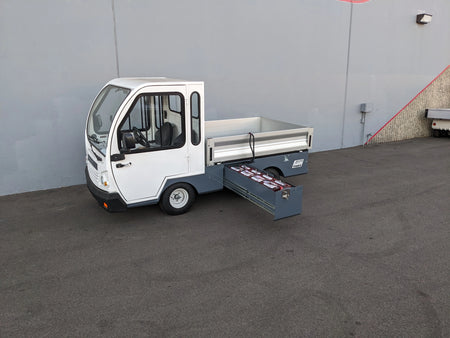 White utility vehicle with an extended battery compartment slide-out drawer showing multiple batteries, featuring the BIGFOOT XL BATTERY SLIDE-OUT RETROFIT FOR TAYLOR-DUNN BIGFOOT XL design.