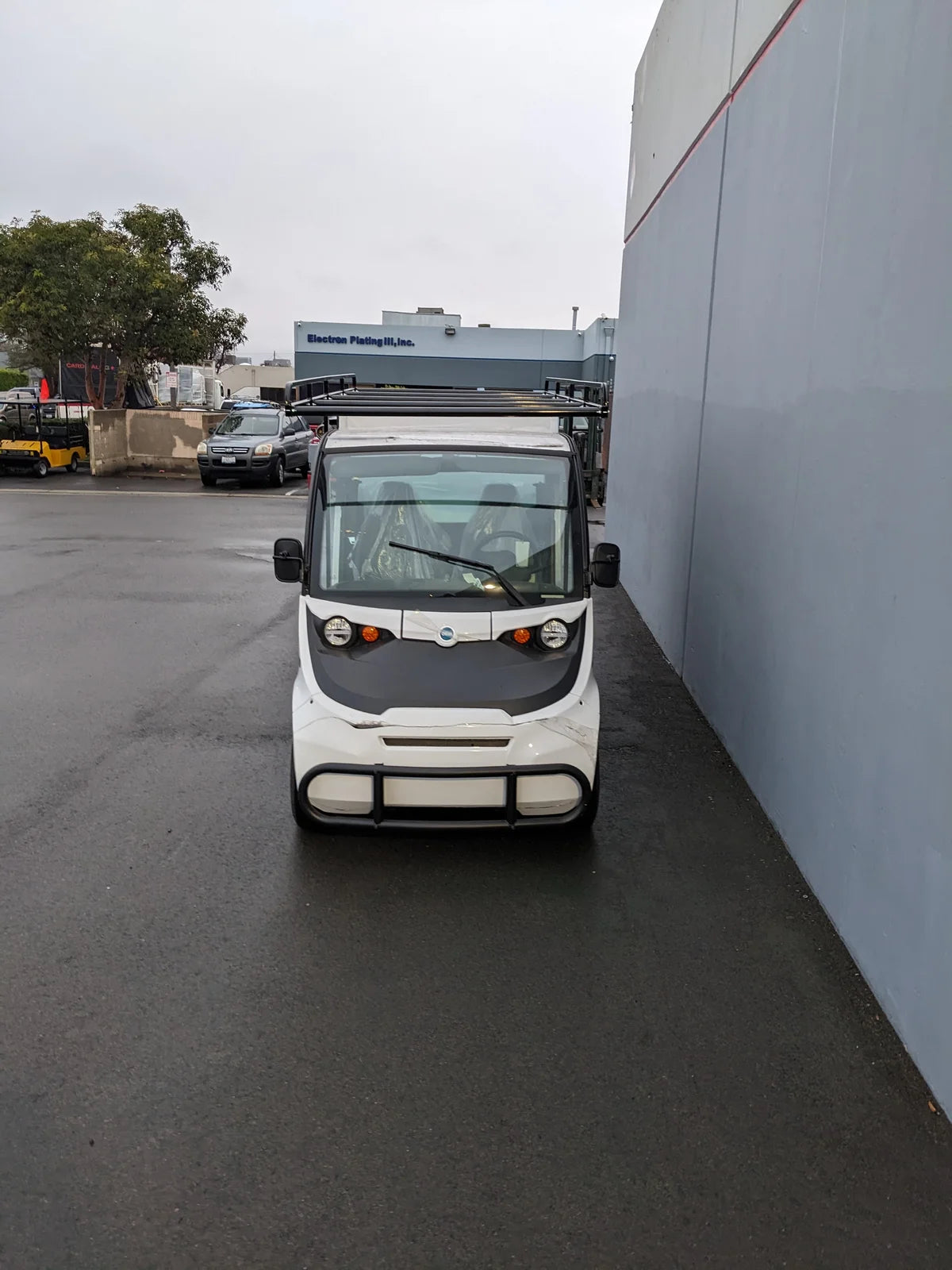 White utility golf cart with roof racks parked next to a building, showcasing custom fabrication for golf carts and compatible with FMB-GEM-52X70X48-S-D3W0 ROLL UP DOORS FLATBED ALUMINUM SMOOTH MULTI-PURPOSE BOX FOR GEM ELXD 52 WIDE X 70 LONG X 48 TALL.