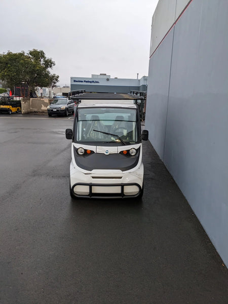 White utility golf cart with roof racks parked next to a building, showcasing custom fabrication for golf carts and compatible with FMB-GEM-52X70X48-S-D3W0 ROLL UP DOORS FLATBED ALUMINUM SMOOTH MULTI-PURPOSE BOX FOR GEM ELXD 52 WIDE X 70 LONG X 48 TALL.