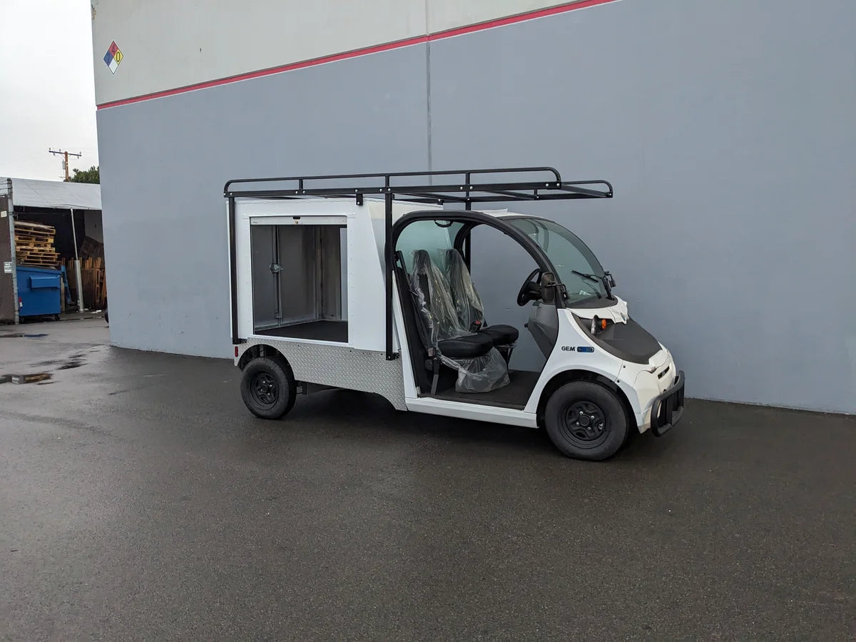 Small white utility golf cart with a custom multi-purpose aluminum box featuring FMB-GEM-52X70X48-S-D3W0 ROLL UP DOORS FLATBED ALUMINUM SMOOTH MULTI-PURPOSE BOX FOR GEM ELXD 52 WIDE X 70 LONG X 48 TALL, designed for custom fabrication for golf carts.
