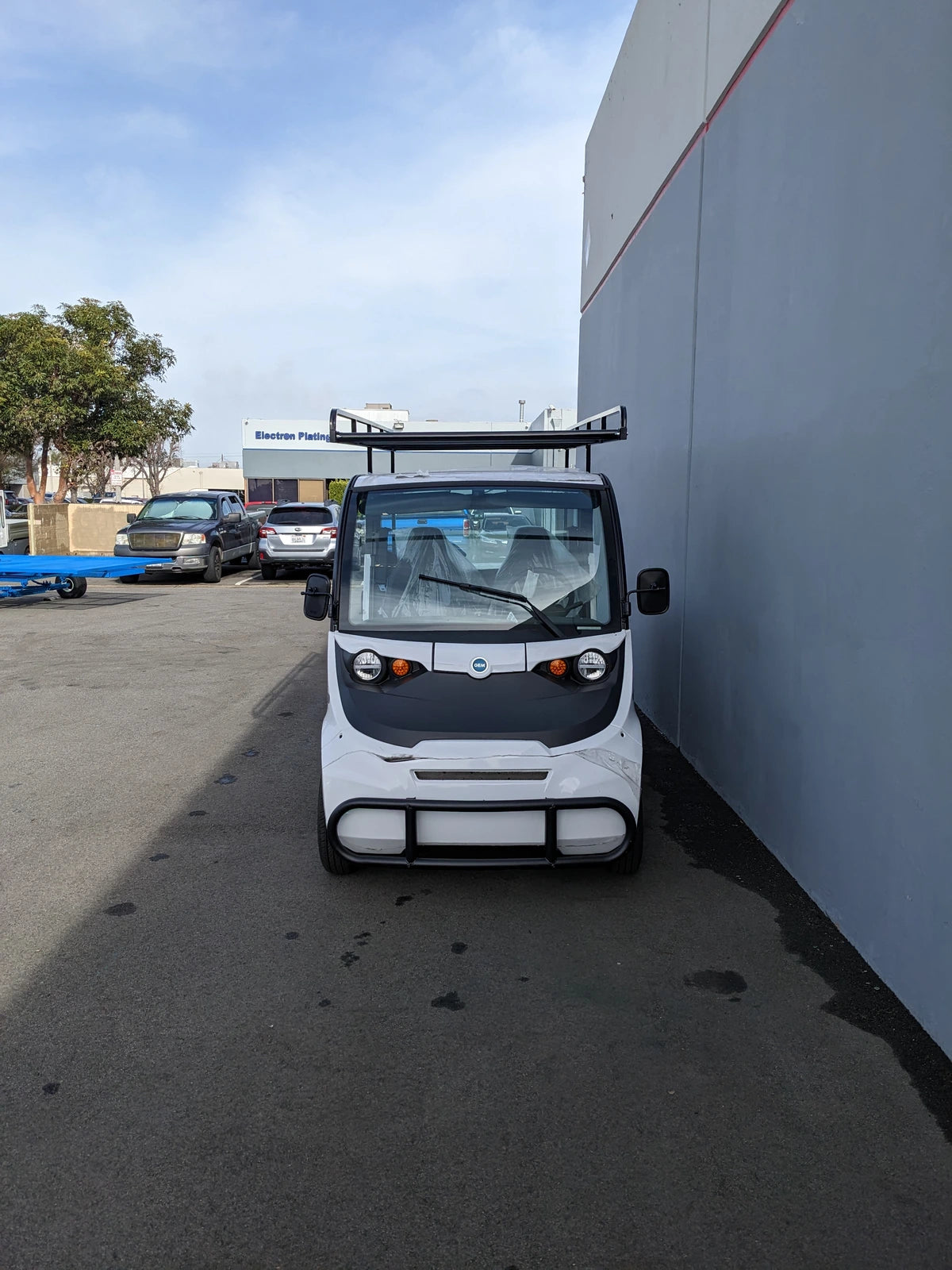 White golf cart parked next to a building featuring DROP RAILS GEM ELXD SOL SOLID SIDE RAILS FOR GEM ELXD, custom fabrication for golf carts enhancing cargo utility racks and accessory support.