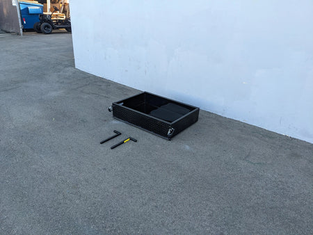 Black heavy-duty metal utility box with open compartments placed on pavement alongside tools, showcasing the EVO-CLASSIC-UTIL31 EVOLUTION CLASSIC HEAVY-DUTY UTILITY BOX designed for custom fabrication for golf carts.