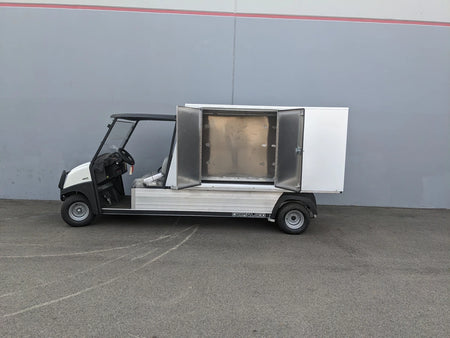 Golf utility vehicle equipped with the CC-CARRYALL900-LAUNDRY BOX FLATBED SPECIFIC PURPOSE BOX FOR CARRYALL 900 WITH LOCKING DOORS, SHELVES, AND HANGING ROD, featuring an open storage compartment.