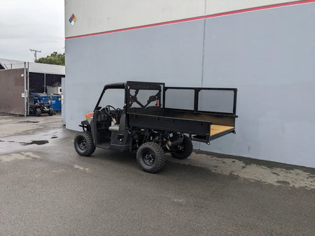 Utility vehicle with a custom flatbed retrofit parked outside a warehouse, featuring the FB-POL-PROXD-54X76X11-STAKE-OCB POLARIS STAKEBED RETROFIT designed for golf carts.