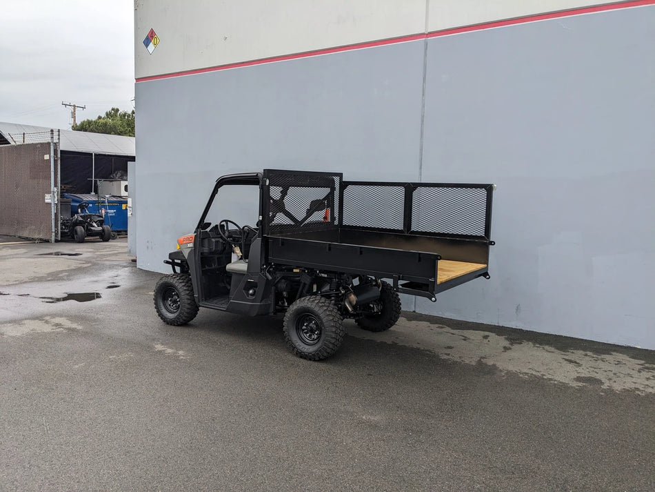 Utility vehicle with a custom flatbed retrofit parked outside a warehouse, featuring the FB-POL-PROXD-54X76X11-STAKE-OCB POLARIS STAKEBED RETROFIT designed for golf carts.