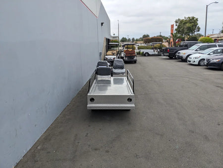 YAM-AMB-2SEAT-REAREMT-96X23 AMBULANCE CART custom fabrication for golf carts with metal platform and two seats parked outdoors near vehicles and buildings.