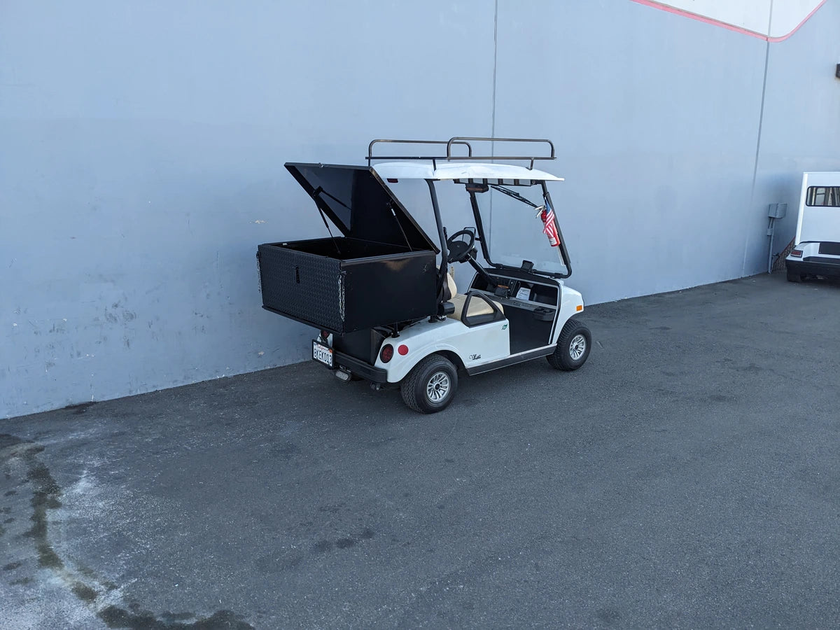 White golf cart equipped with a black CC-VILL-CARGO31 LOCKING CARGO BOX FOR CLUB CAR VILLAGER mounted on the back, custom fabricated for secure utility cargo transport.