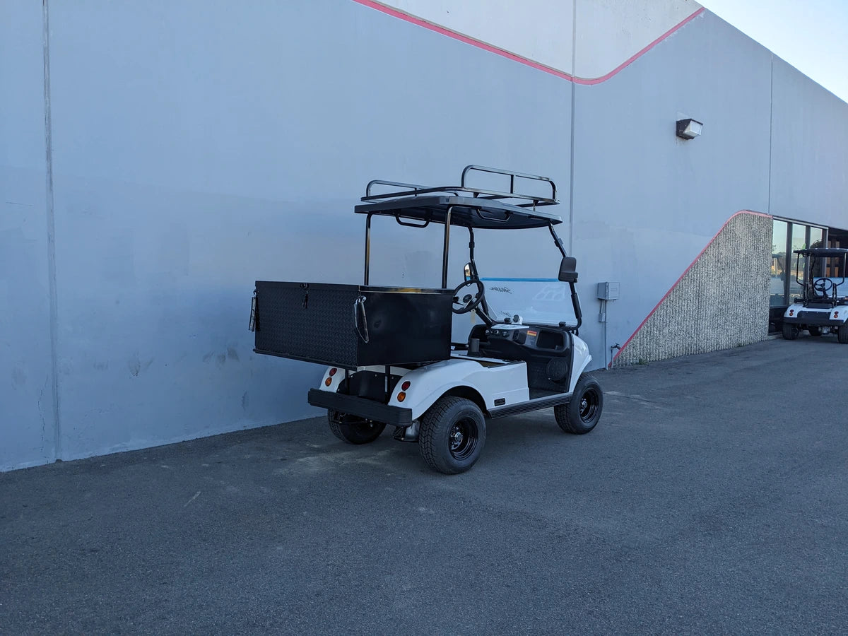 White golf cart equipped with EVO-CLASSIC2-50LR EVOLUTION CLASSIC 2 LADDER RACK featuring custom fabrication for golf carts, parked beside a gray building under daylight.