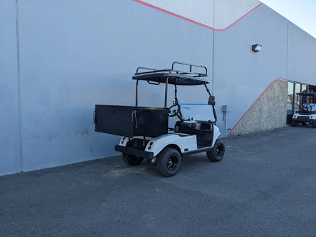 White golf cart equipped with EVO-CLASSIC2-50LR EVOLUTION CLASSIC 2 LADDER RACK featuring custom fabrication for golf carts, parked beside a gray building under daylight.