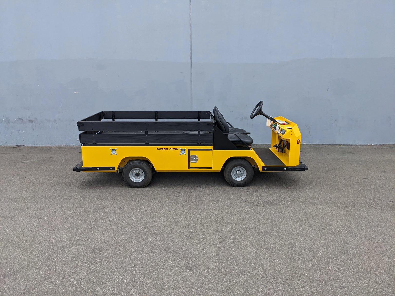 BIGFOOT-DOOR-COMPARTMENT Pass Through Storage Cabinet for Taylor Dunn Bigfoot installed on a yellow utility cart hauler with flatbed cargo area and black railing.