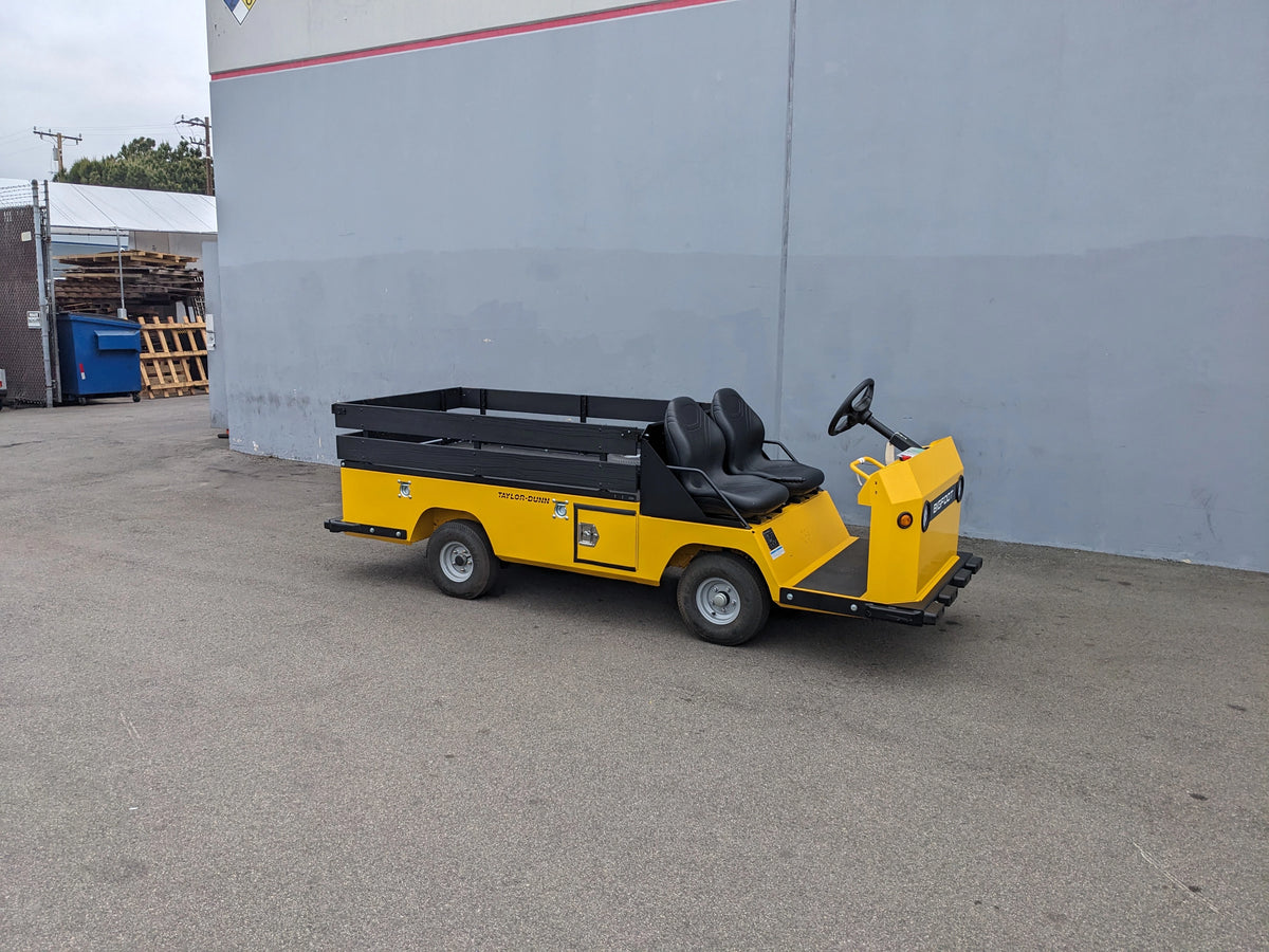 Yellow utility cart with two black seats and a flatbed storage area attached, featuring the BIGFOOT-DOOR-COMPARTMENT Pass Through Storage Cabinet for Taylor Dunn Bigfoot designed for cargo and utility use.