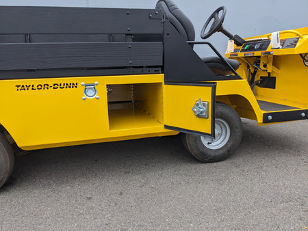 BIGFOOT-DOOR-COMPARTMENT Pass Through Storage Cabinet for Taylor Dunn Bigfoot shown open on a yellow utility vehicle with black seating and wooden side panels.