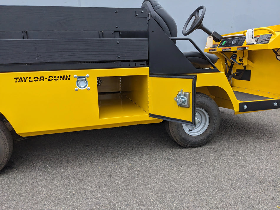 BIGFOOT-DOOR-COMPARTMENT Pass Through Storage Cabinet for Taylor Dunn Bigfoot shown open on a yellow utility vehicle with black seating and wooden side panels.