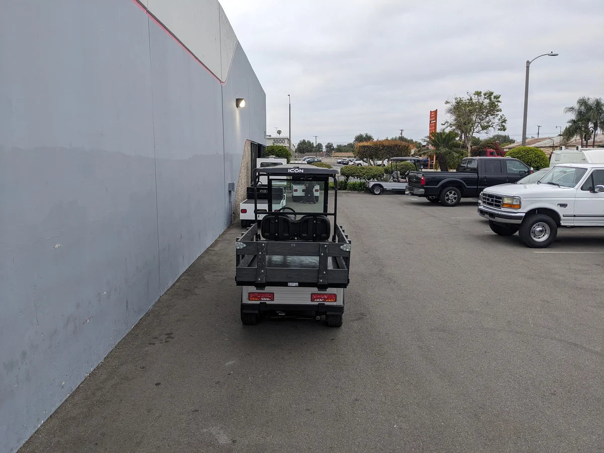 Golf cart with STAKE-SIDES-44X72X18-COMP Flatbed Golf Cart Composite Stake Sides installed, showcasing custom fabrication for golf carts in a parking lot with trucks and building nearby.