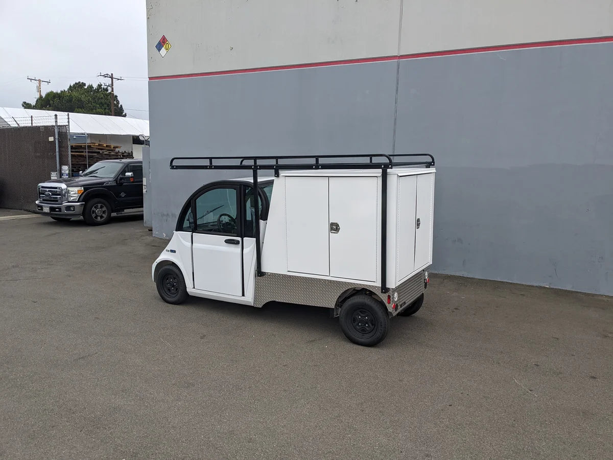 Small white utility golf cart equipped with custom fabrication including GEM-ELXD-53X120-TLR Top Mount Ladder Rack for outside mount on a GEM ELXD, featuring enclosed cargo compartments and black wheels.