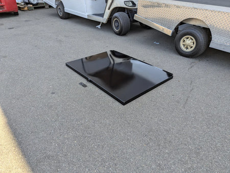 Black retrofit locking lid for cart haulers utility boxes labeled UTIL31-LID RETROFIT LOCKING LID FOR CART HAULERS UTILITY BOXES, custom fabricated for golf carts, placed on ground near utility vehicles.
