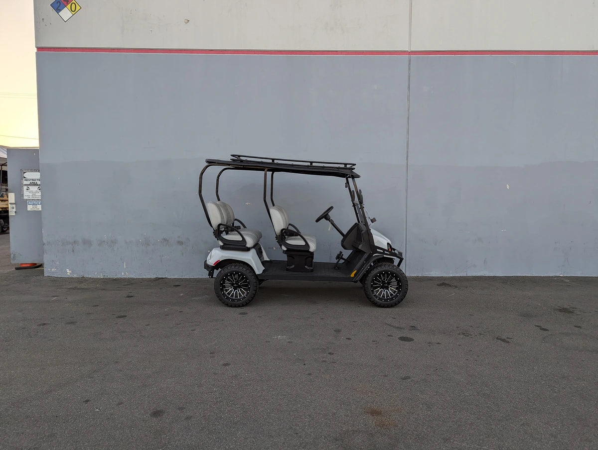 White and black golf cart equipped with the EZGO-LIBERTY-64RR3 EZ GO LIBERTY ROOF RACK in a warehouse setting, showcasing custom fabrication for golf carts.