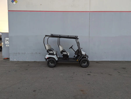White and black golf cart equipped with the EZGO-LIBERTY-64RR3 EZ GO LIBERTY ROOF RACK in a warehouse setting, showcasing custom fabrication for golf carts.