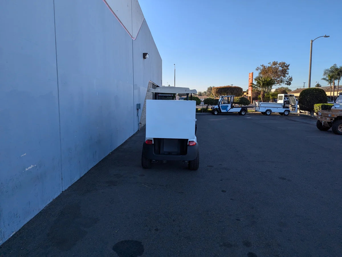 TB-36X18X28-FH BED MOUNT TOOLBOX WITH HINGED DOOR mounted on the back of a golf cart in an outdoor parking area, featuring custom fabrication for golf carts.