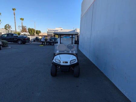 White golf cart parked outdoors next to a building, featuring a custom fabricated TB-36X18X28-FH BED MOUNT TOOLBOX WITH HINGED DOOR designed for golf cart accessory cargo and utility storage.