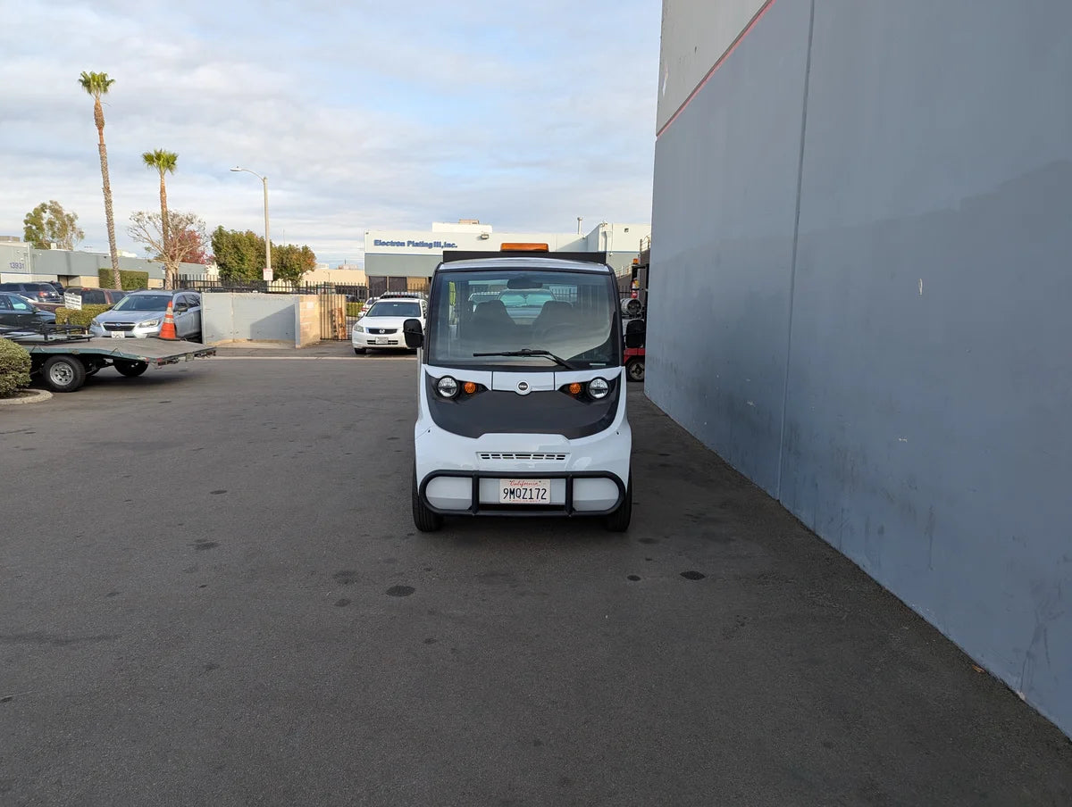 White compact golf cart parked next to a building, showcasing the GEM-E6 WHEELCHAIR TRANSPORT GEM GOLF CART CONVERSION FOR WHEELCHAIR PASSENGER with custom fabrication for golf carts.
