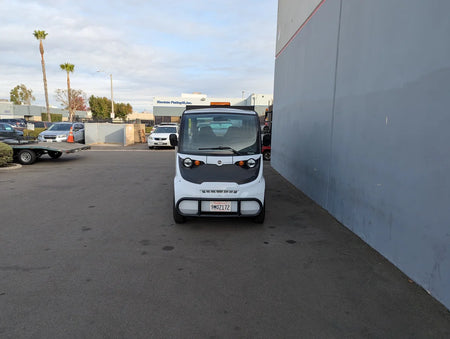 White compact golf cart parked next to a building, showcasing the GEM-E6 WHEELCHAIR TRANSPORT GEM GOLF CART CONVERSION FOR WHEELCHAIR PASSENGER with custom fabrication for golf carts.