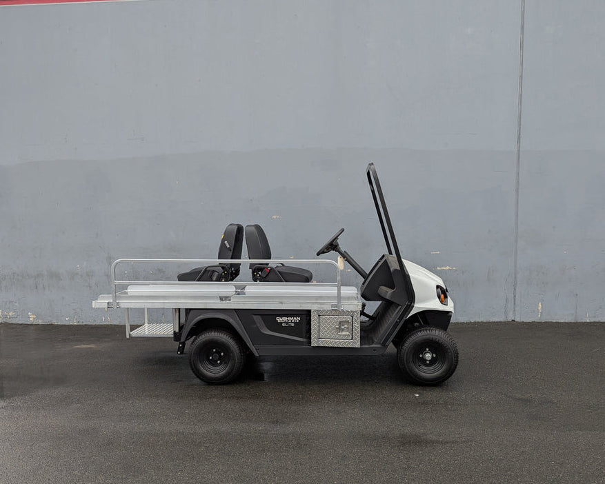 Side view of a white golf cart equipped with a custom fabricated CUSH-EMT-84X24 EMT GOLF CART BED CONVERSION FOR CUSHMAN GOLF CART featuring a flatbed, utility boxes, and seating for two.
