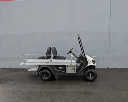 Side view of a white golf cart equipped with a custom fabricated CUSH-EMT-84X24 EMT GOLF CART BED CONVERSION FOR CUSHMAN GOLF CART featuring a flatbed, utility boxes, and seating for two.