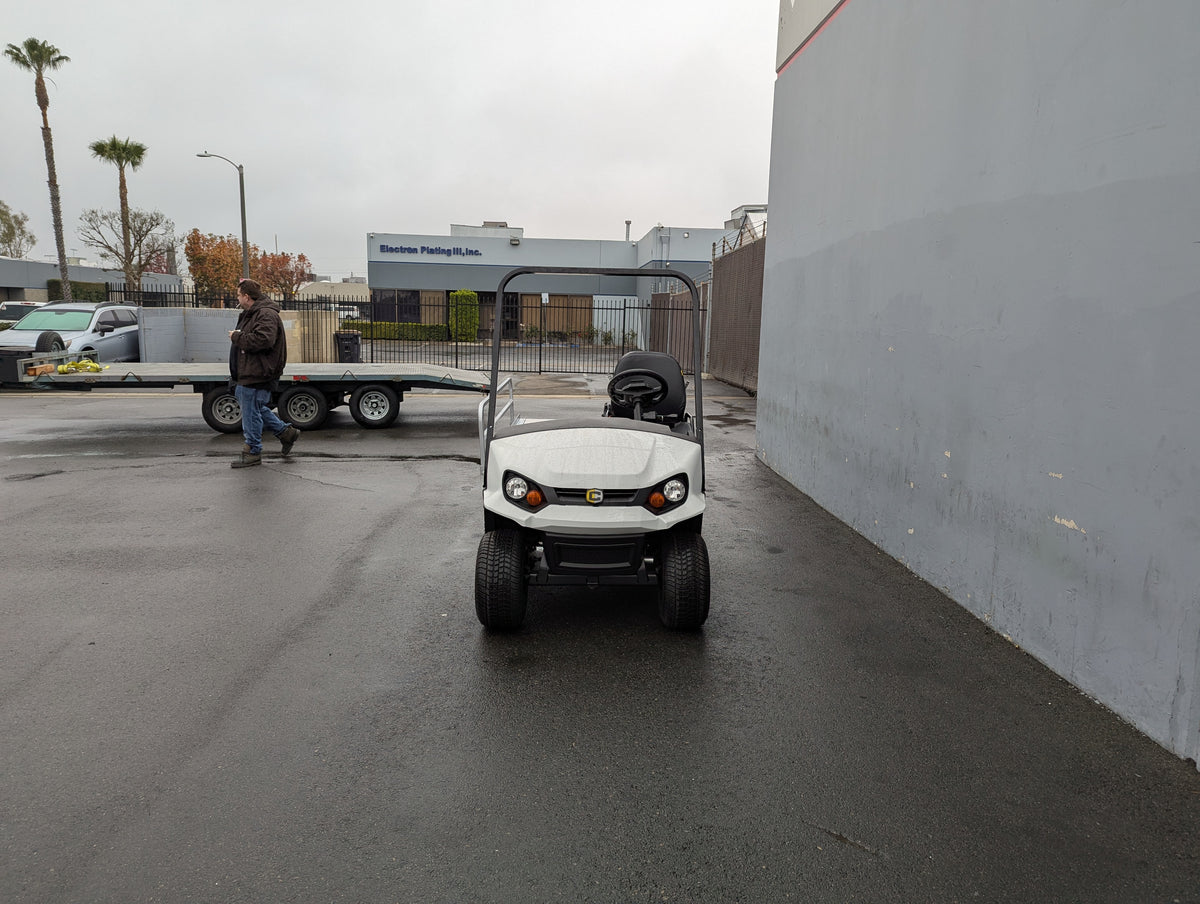 White golf cart equipped with CUSH-EMT-84X24 EMT GOLF CART BED CONVERSION FOR CUSHMAN GOLF CART, showcasing custom fabrication for golf carts in an outdoor industrial setting.