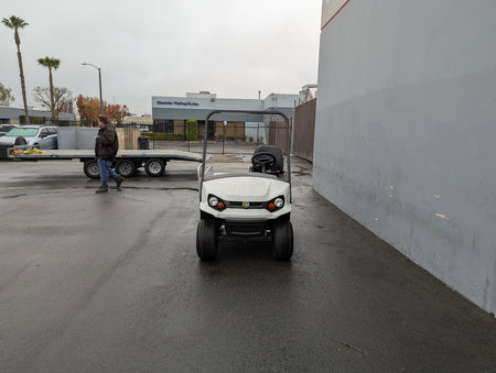 White golf cart equipped with CUSH-EMT-84X24 EMT GOLF CART BED CONVERSION FOR CUSHMAN GOLF CART, showcasing custom fabrication for golf carts in an outdoor industrial setting.