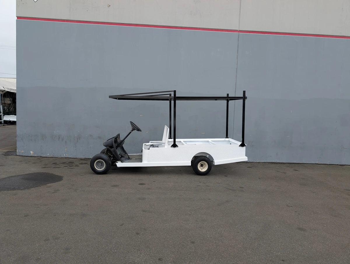 White custom flatbed golf cart with black FB-45X120-TLR FLATBED TOP LADDER RACK, 45″ X 120″ WITH REMOVABLE REAR CROSS BAR installed, designed for carrying ladders and cargo.