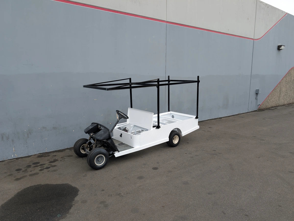 White custom flatbed golf cart with black metal frame installed, featuring FB-45X120-TLR FLATBED TOP LADDER RACK, 45″ X 120″ WITH REMOVABLE REAR CROSS BAR for hauling ladders and cargo.