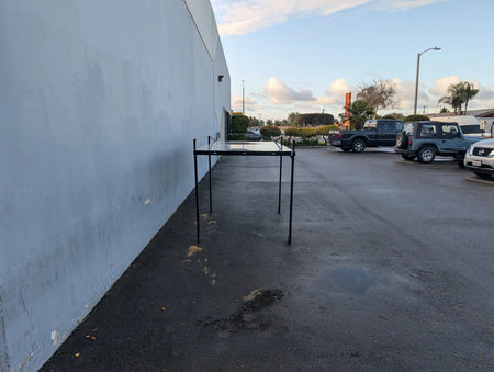 FB-45X120-TLR DECK 10 FT Top Mount Ladder Rack for Flatbed with Solid Deck displayed outdoors near a building wall, showcasing sturdy metal construction for custom fabrication for golf carts.